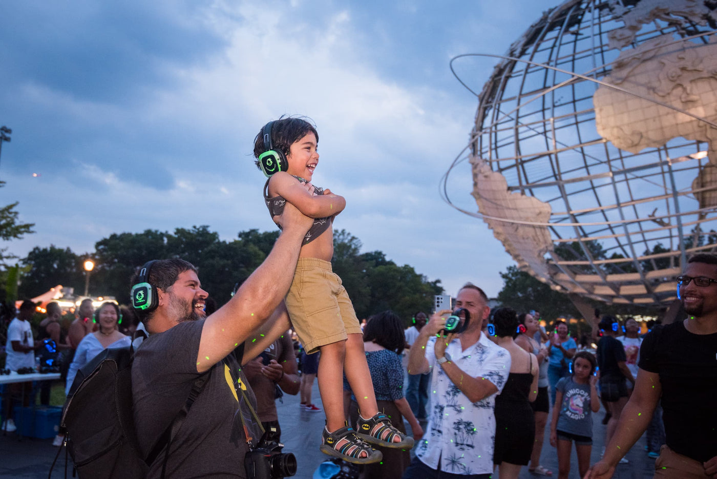 Quiet Events Silent Disco headphones for kids.  A Dad lifts his son in front of him up in the air at the park.