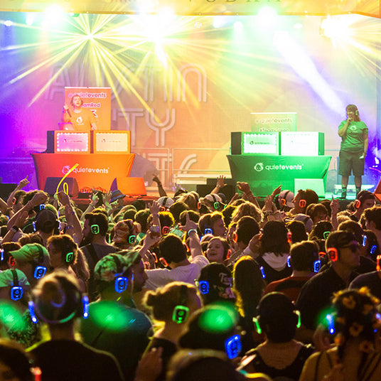 Quiet Events Silent Disco headphones for fairs a group of people dancing with headphones on the dance floor and DJ's on stage playing music