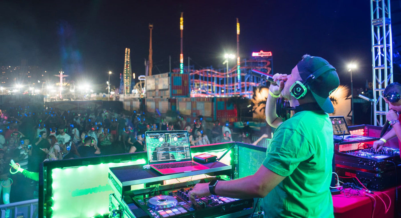 Quiet Events Silent Disco headphones for fairs a DJ on state speaking on the mic to the crowd at night in an amusement park.