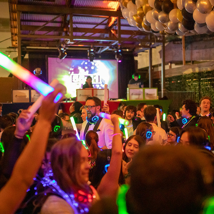 Quiet Events Silent Disco headphones for Austin.  A group of people dancing having fun on a dance floor with three DJ's on a stage wearing headphones.