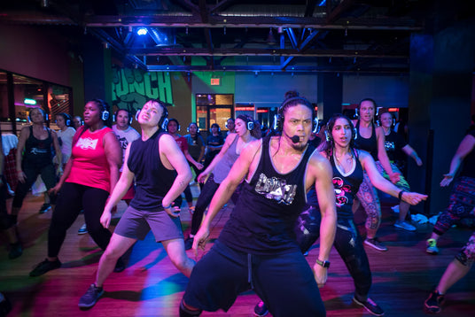 Quiet Events Silent Disco headphones for all ages.  A group of gym members taking a dance class with an instructor ahead of the class.