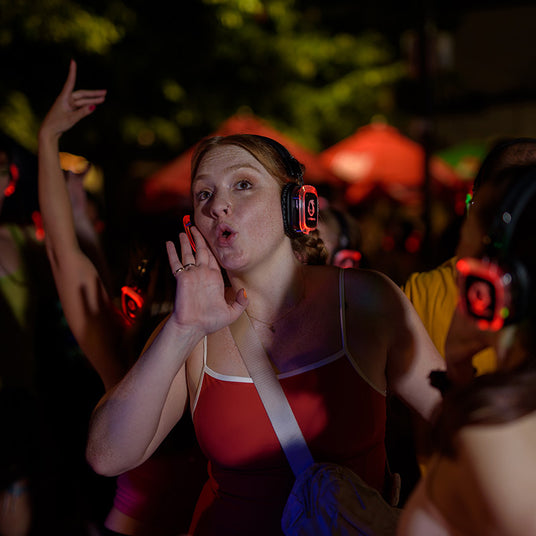 Quiet Events Silent Disco headphones for camps.  A single girl wearing headphones with people and trees in the background.