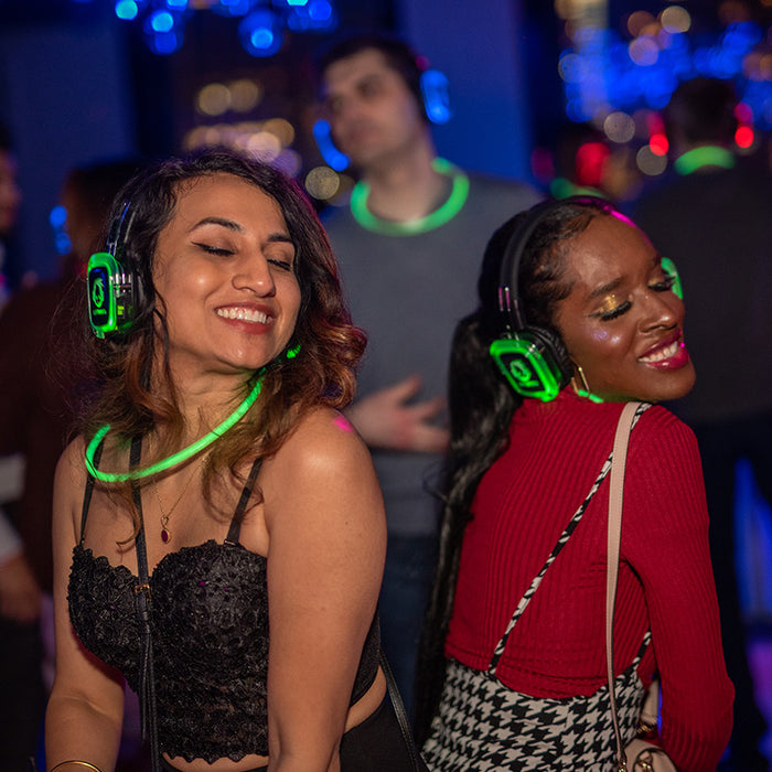 Quiet Events Silent Disco headphones for city party tours.  Two girls having fun back to back smiling, because of the music they are listening with headphones.
