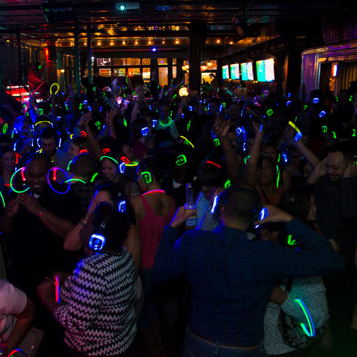 Quiet Events Silent Disco headphones for concerts.  A group of people having fun and dancing in a close less lighting space using headphones.