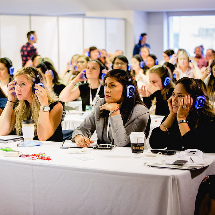 Quiet Events Silent Disco headphones for conferences a group of women wearing headphones sitting behind tables paying attention like in a workshop.