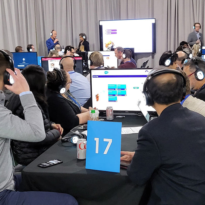 Quiet Events Silent Disco headphones for conferences a group people sitting and wearing headphones listening at a workshop with screens.