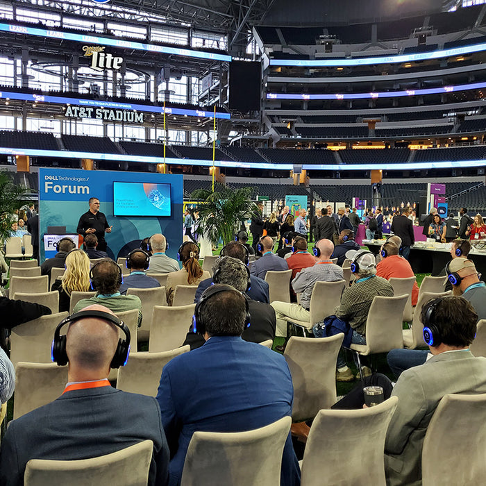 Quiet Events Silent Disco headphones for conferences a group of people wearing headphones and sitting listening to a speaker in a open forum.