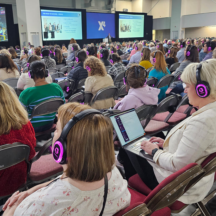 Quiet Events Silent Disco headphones for conferences a large group of people wearing headphones paying attention to large screens.