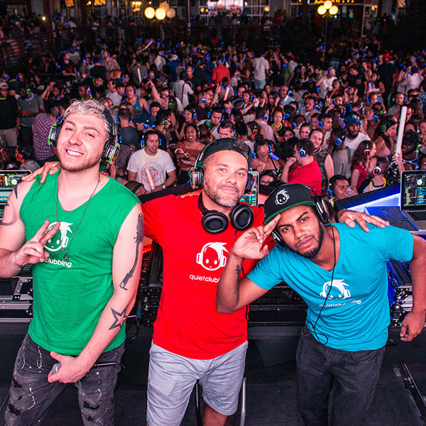 Quiet Events Silent Disco headphones for dance parties three DJ's posing on stage with fans on the background.