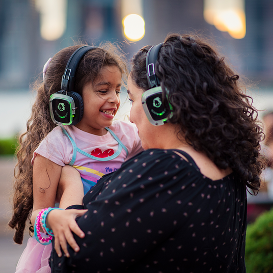 Quiet Events Silent Disco headphones for kids.  A daughter and her mother looking at each other eyes enjoying and having fun with headphones.
