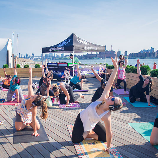 Quiet Events Silent Disco headphones for fitness and wellness.  A yoga instructor with her students outdoors wearing headphones and posing.
