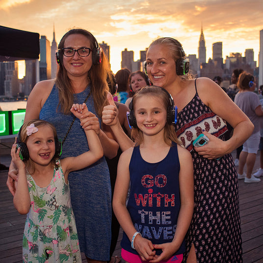 Quiet Events Silent Disco headphones for fund raising.  Two mothers and their children at an outdoor event having fun with headphones.