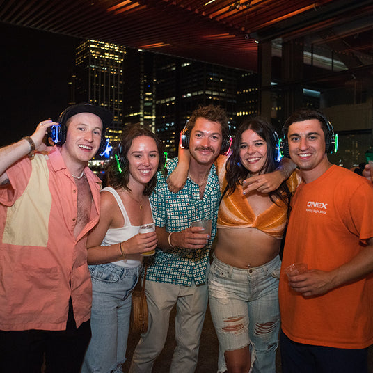 Quiet Events Silent Disco headphones for hotels.  A group of four people gather together at a party having fun and wearing headphones.
