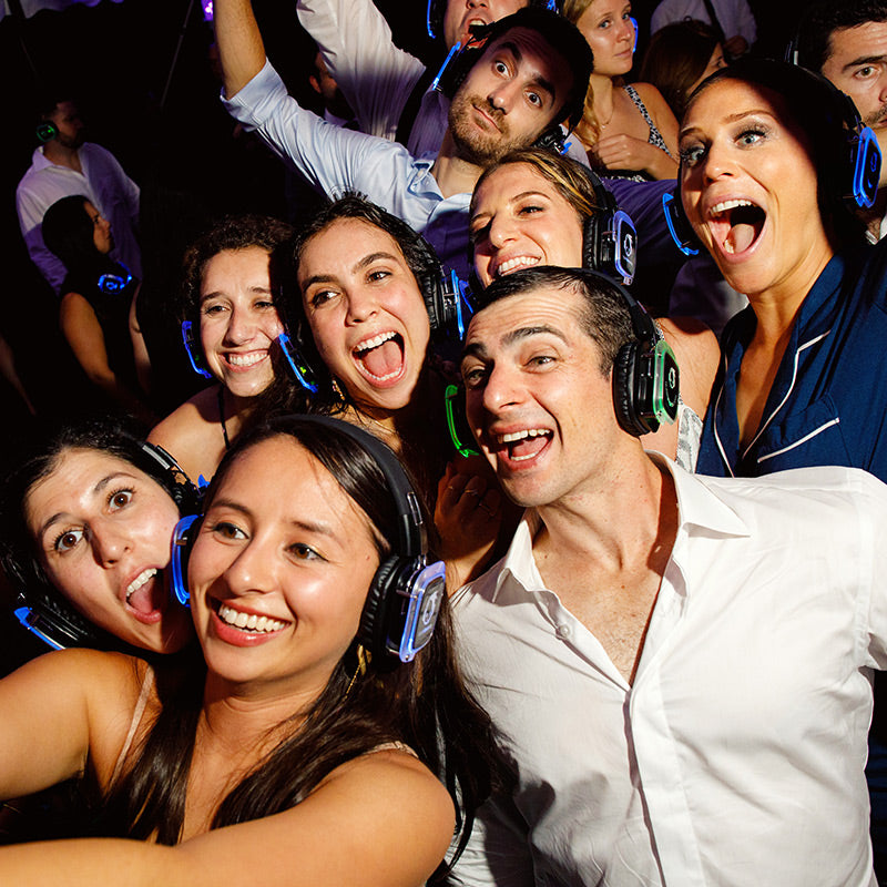 Quiet Events Silent Disco headphones for hotels.  A group of people gather together smiling and posing for a picture with headphones.