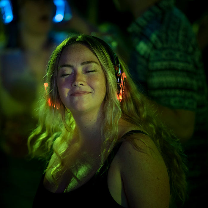 Quiet Events Silent Disco headphones for listening party.  A woman with her eyes closed smiling with red party headphones.