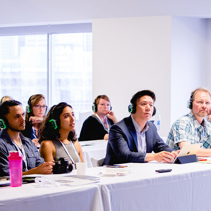 Quiet Events Silent Disco headphones for meetings a group of people sitting with headphones listening to a speaker.
