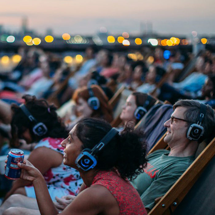 Quiet Events Silent Disco headphones for movies.  A group of people sitting on relax chairs at an outdoor event watching a movie with headphones.