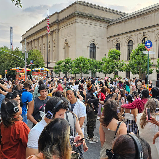 Quiet Events Silent Disco headphones for museums.  A group of people standing outside a museum during the day wearing headphones.