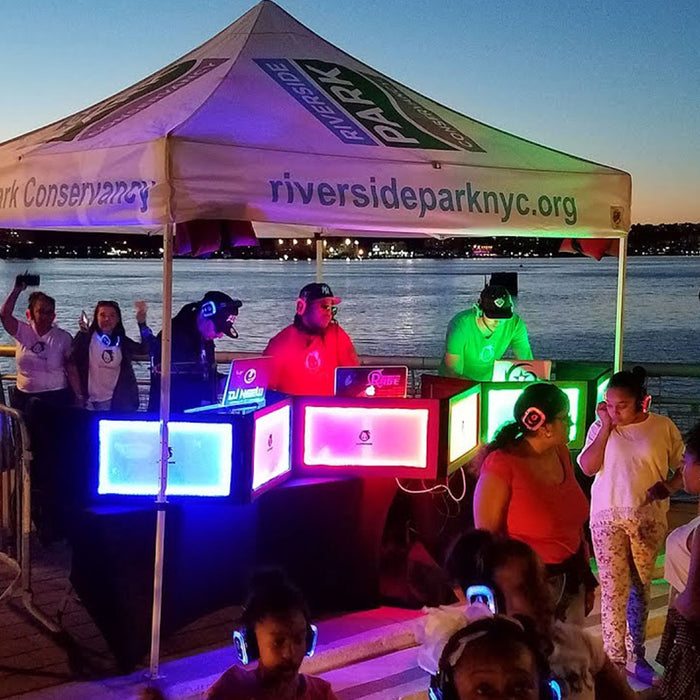 Quiet Events Silent Disco headphones for parks.  A group of DJ's underneath a tent outdoors playing music for others.
