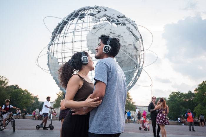 Quiet Events Silent Disco headphones for parks.  A happy couple dancing at park with a large Sphere in the background. 