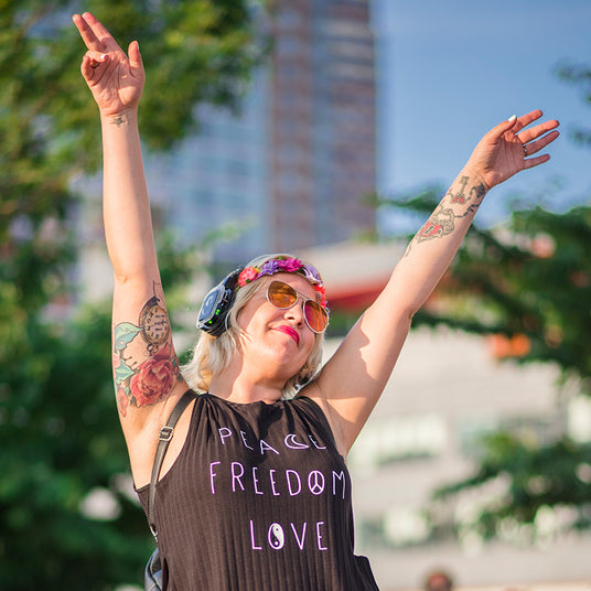 Quiet Events Silent Disco headphones for property management.  A young woman outdoors enjoying her time in the sun with her hands up in the air wearing headphones.