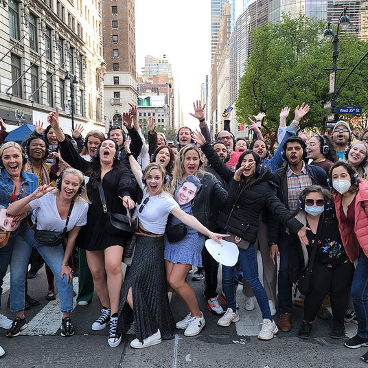 Quiet Events Silent Disco headphones for schools and universities.  A group of people gather together cheering with their hands up having fun and headphones.