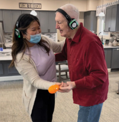Quiet Events Silent Disco headphones for senior care.  A senior man being entertained by an assistant holding hands and wearing headphones.