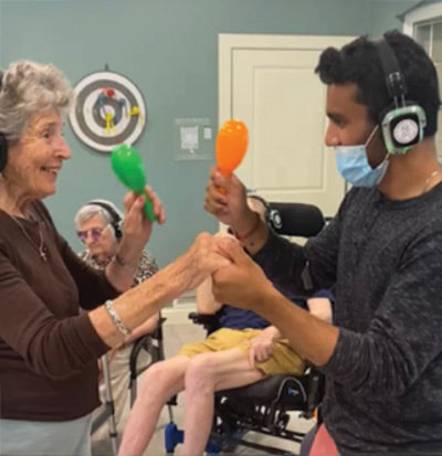 Quiet Events Silent Disco headphones for senior care.  An older woman with an assistant having fun holding hands wearing headphones.