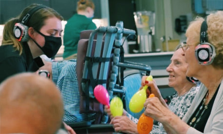 Quiet Events Silent Disco headphones for senior care.  A group of older women having fun and being assisted and wearing headphones.