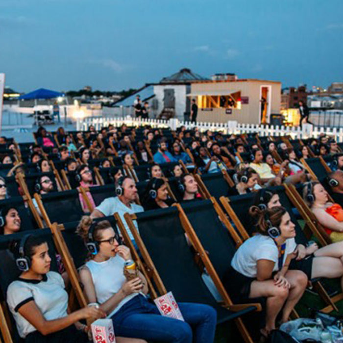 Quiet Events Silent Disco headphones for theater and plays.  A group of people together sitting in an outdoor space watching a screen.