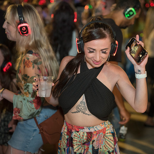 Quiet Events Silent Disco headphones for traveling.  A young woman dancing and having fun outdoors with others wearing headphones.