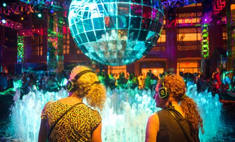 Two people looking up at a disco ball wearing glowing headphones at a silent disco